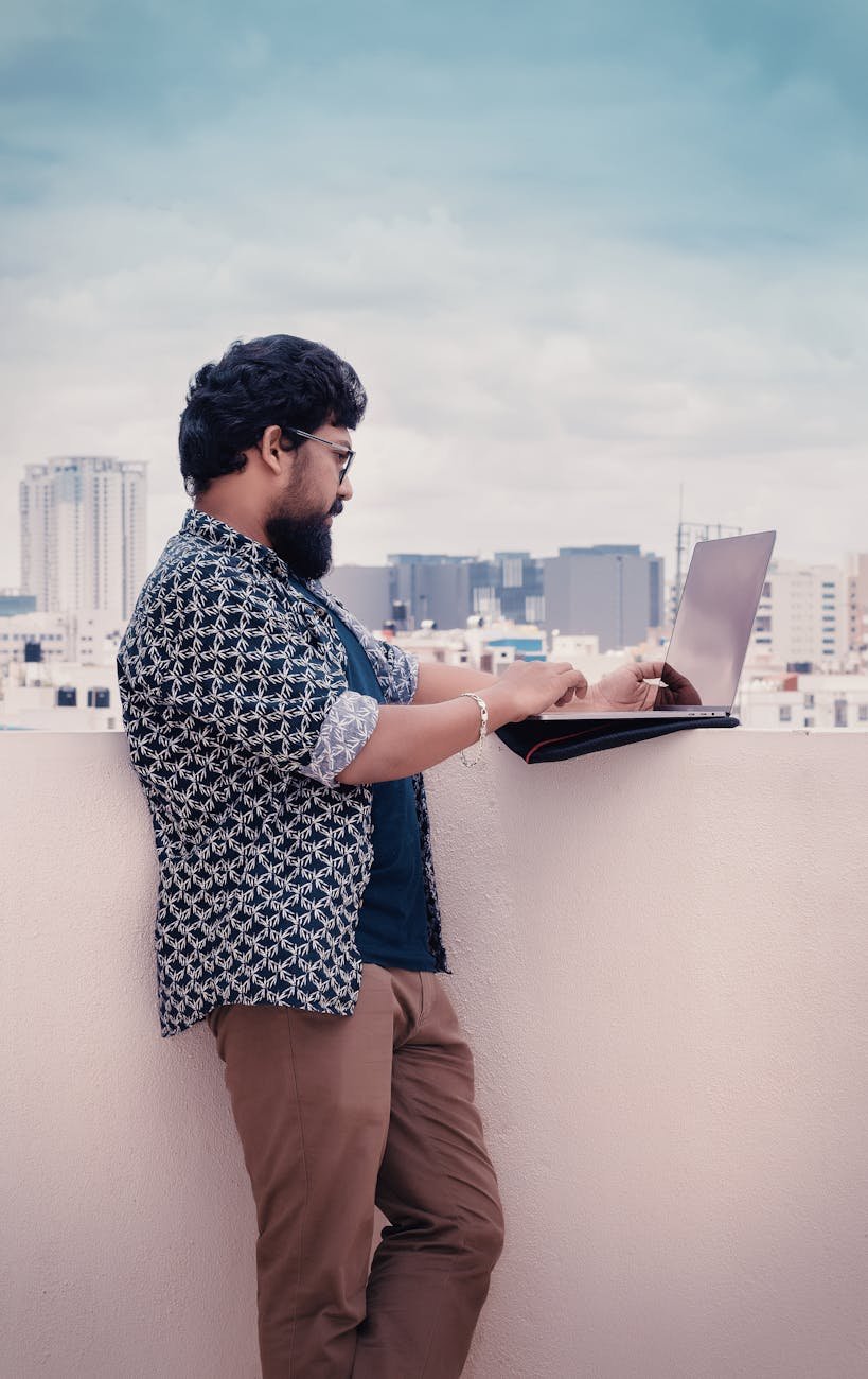 man standing beside white wall holding laptop computer