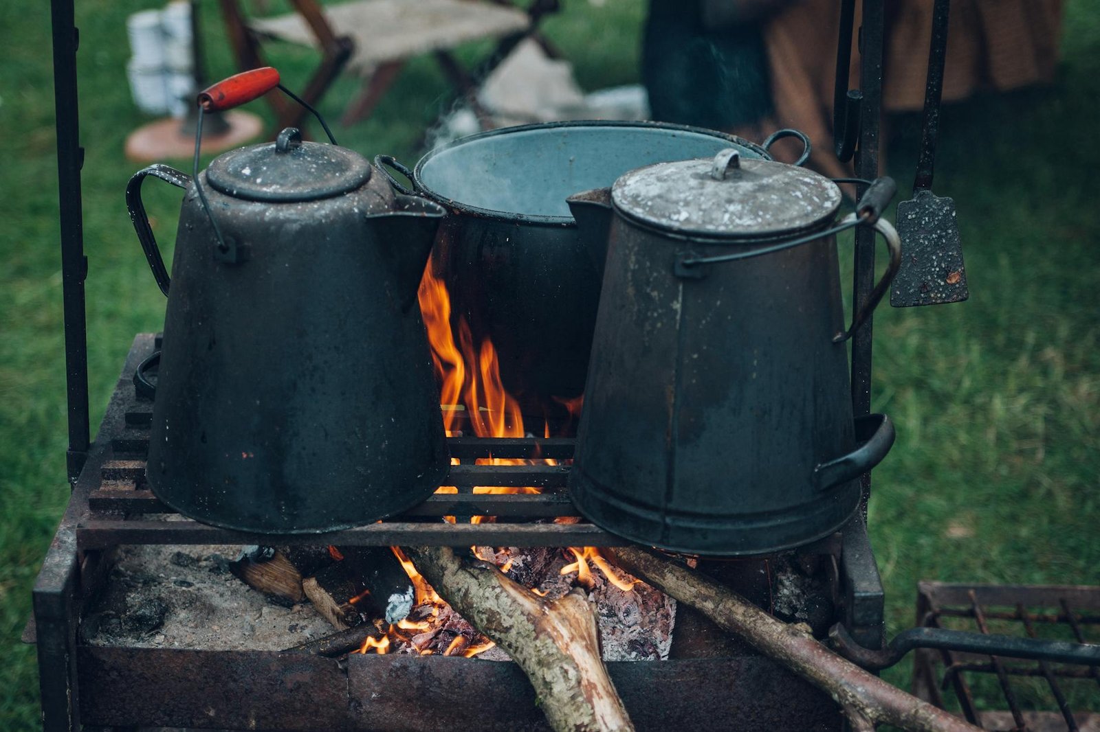 three black and gray pots on top of grill with fire on focus photo